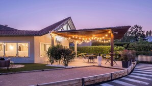 Una casa moderna con un porche cubierto, mobiliario exterior y luces colgantes.