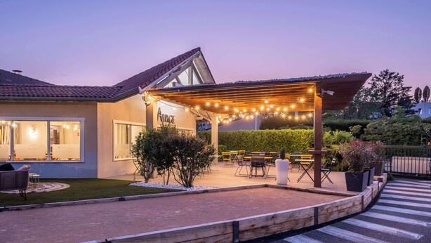 Ein modernes Haus mit überdachter Terrasse, Sitzgelegenheiten im Freien und Lichterketten.