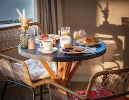 Una mesa de desayuno con diversas comidas y bebidas, rodeada de sillas de mimbre.