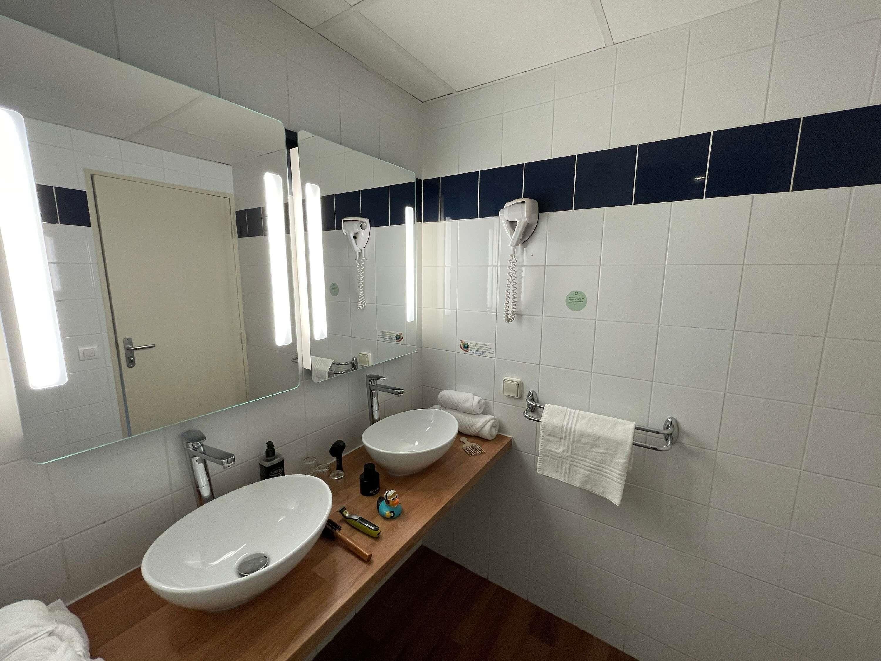 A bathroom with a large mirror, two sinks, a towel rack, and a hairdryer.