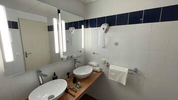 A bathroom with a large mirror, two sinks, a towel rack, and a hairdryer.