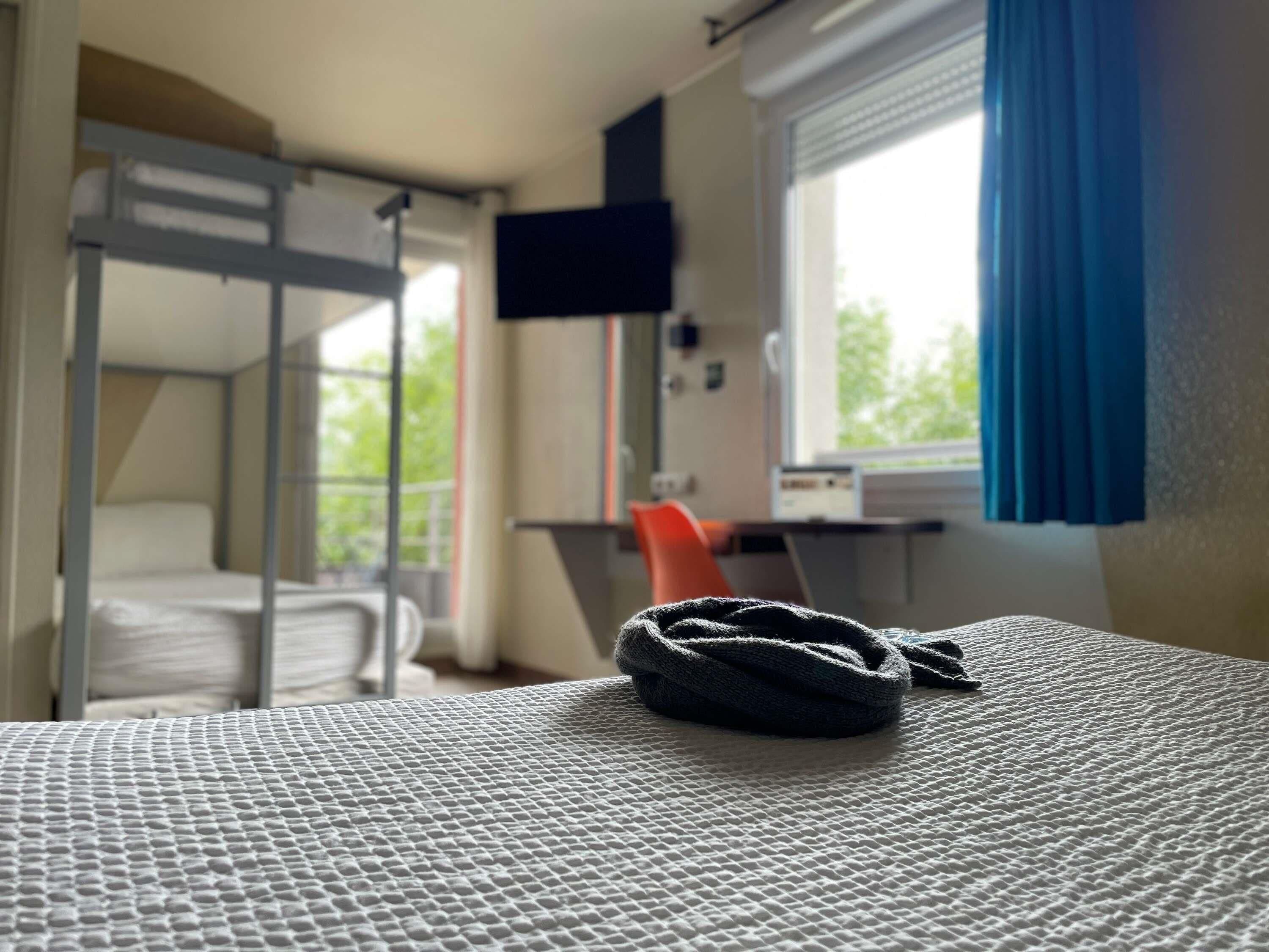 A bunk bed room with a television on the wall, a window with curtains, and a desk with a chair.