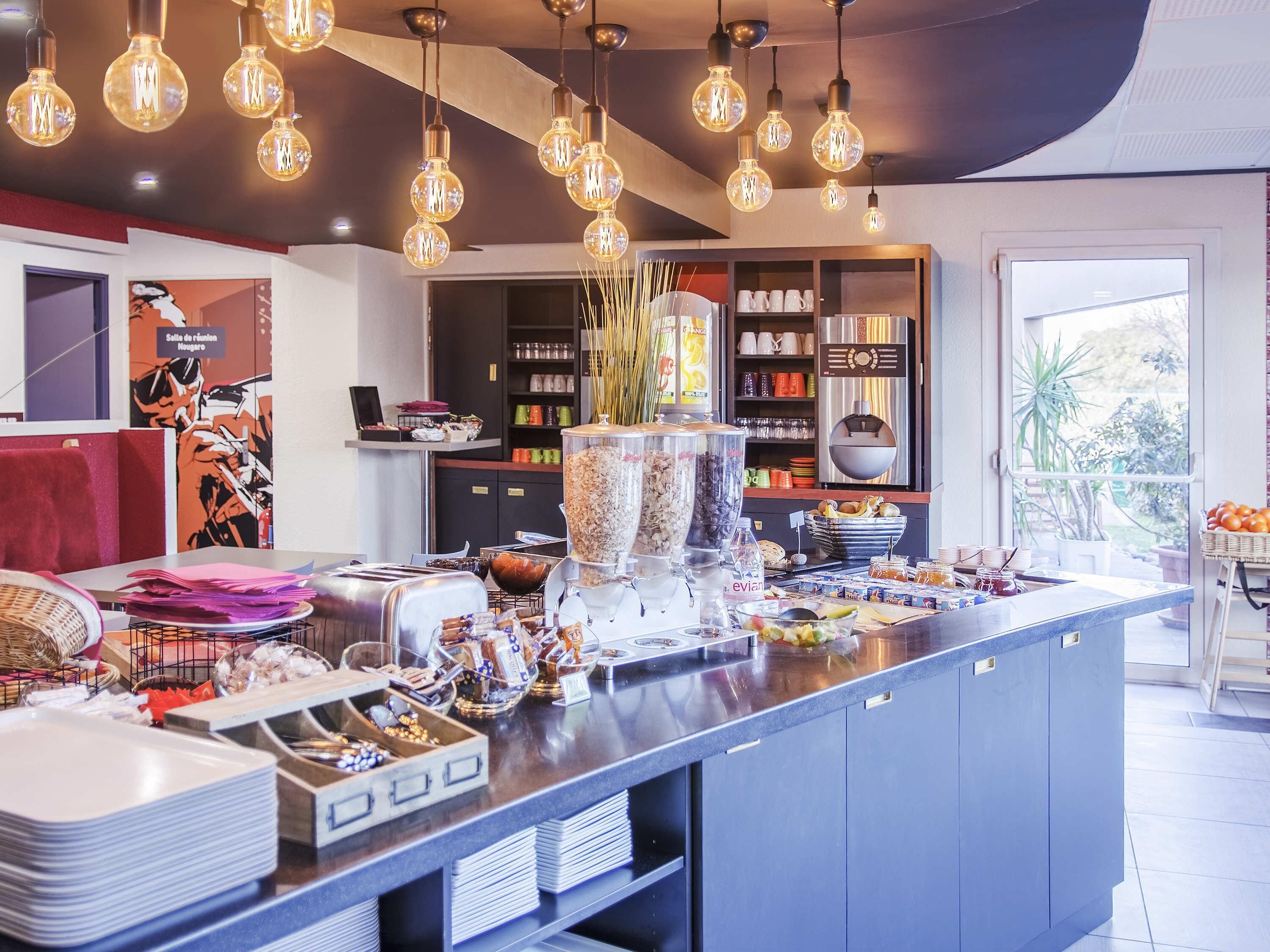 A modern kitchen with a central island, hanging light fixtures, and a view of the outdoors.