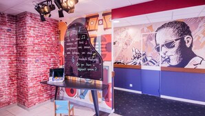 A room with a brick wall, a table with a laptop, and a mural with musical notes and a face. - ibis Styles Toulouse Blagnac Aeroport (Blagnac)