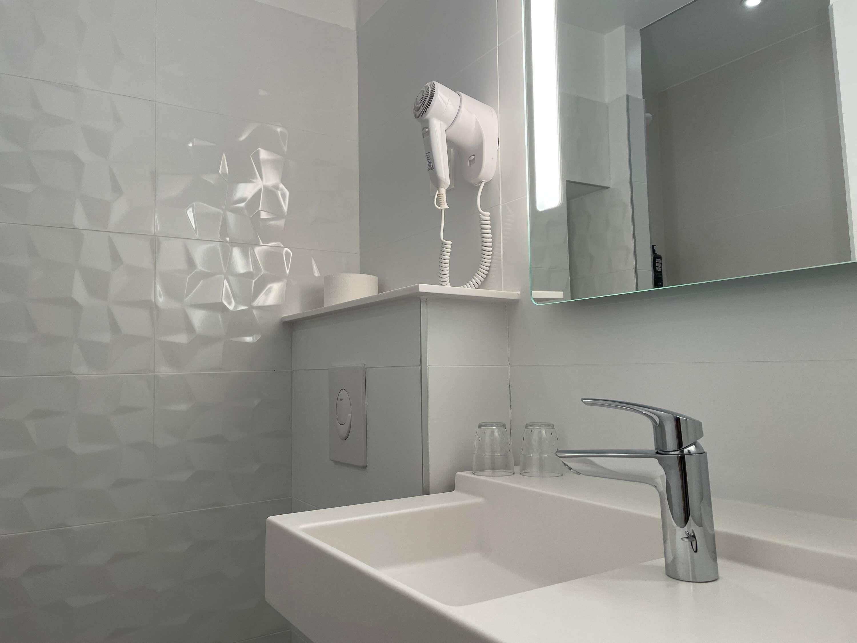 A modern bathroom with a white sink, a mirror, and a hairdryer on a shelf.