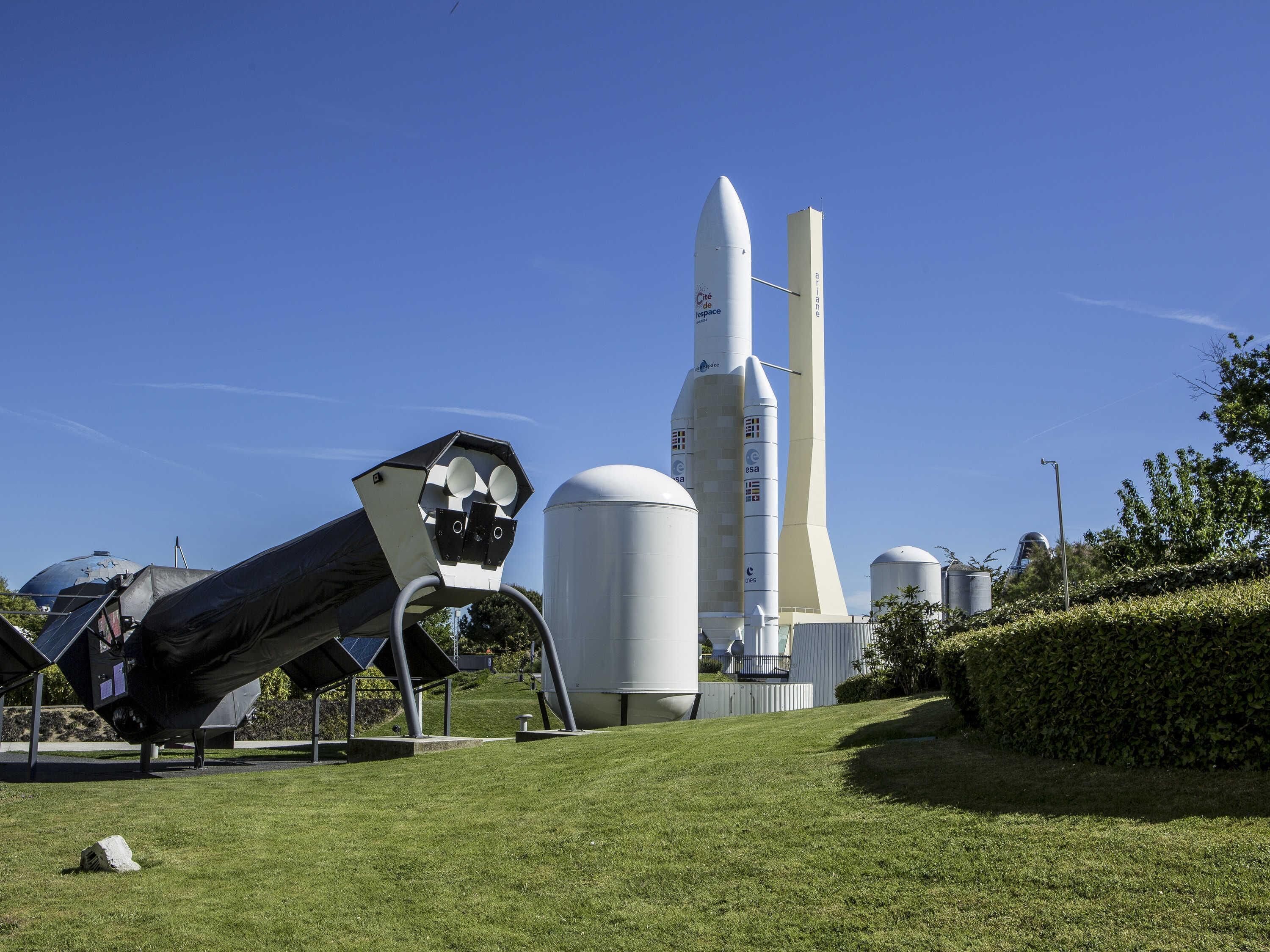 Un transbordador espacial en exhibición, con un gran telescopio y estructuras cilíndricas al fondo.