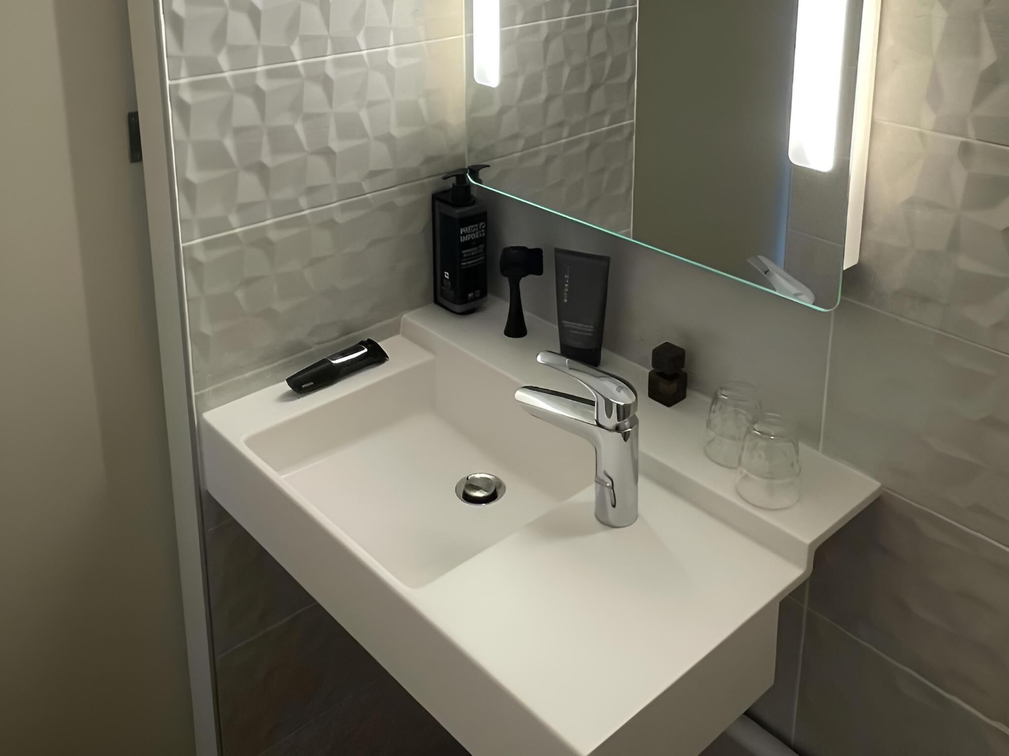 Un baño moderno con un lavamanos blanco, un grifo de cromo y un estante de vidrio con artículos de aseo.