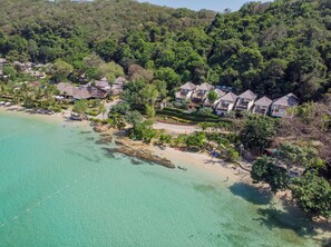 An aerial view of a coastal resort with multiple bungalow-style houses, a sandy beach, and clear turquoise waters. - Le Vimarn Cottages & Spa (Rayong)
