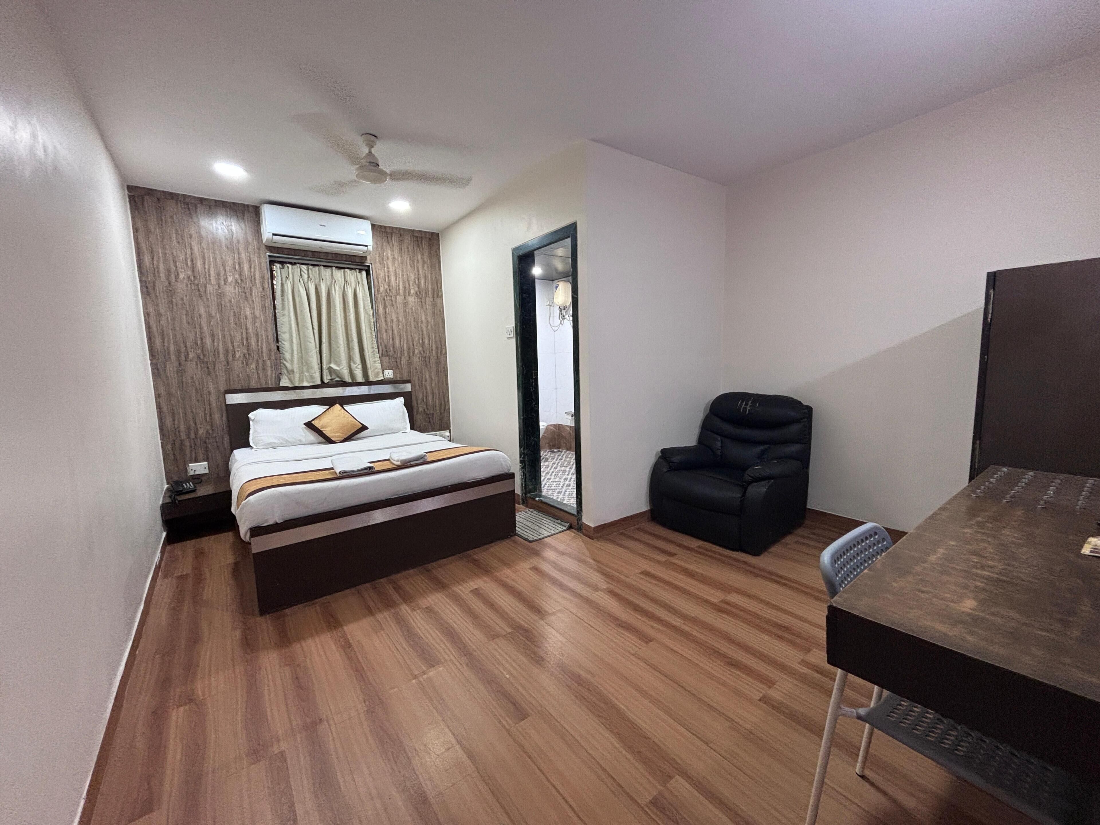 A bedroom with a bed, a chair, a desk, a ceiling fan, and an air conditioning unit.