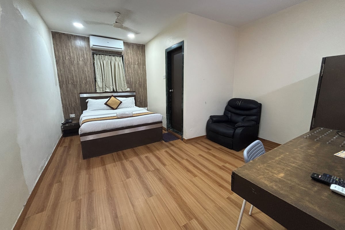 A hotel room with a bed, a desk with a chair, a black leather chair, a ceiling fan, and an air conditioning unit.