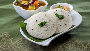 Ein Teller mit zwei Idlis und zwei kleinen Schälchen Chutney und Sambar.