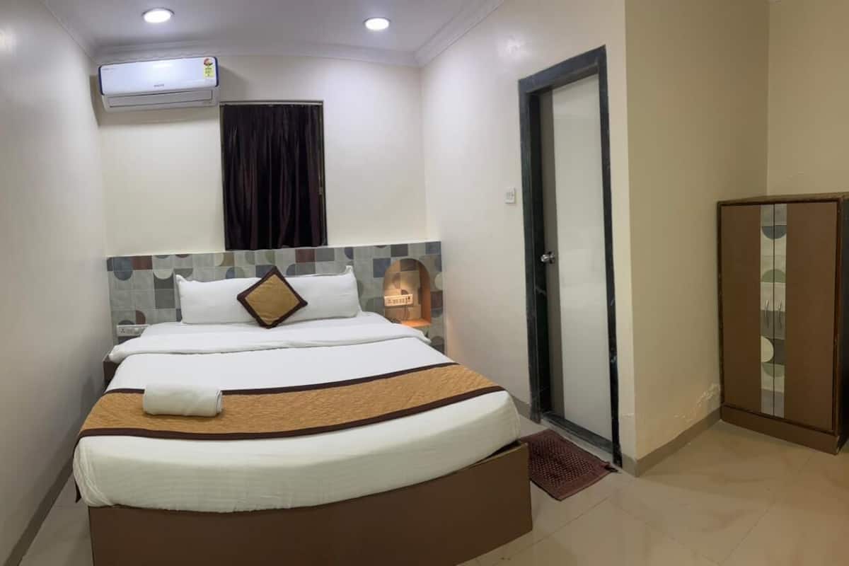 A hotel room with a bed, an air conditioning unit, a wardrobe, and a door.
