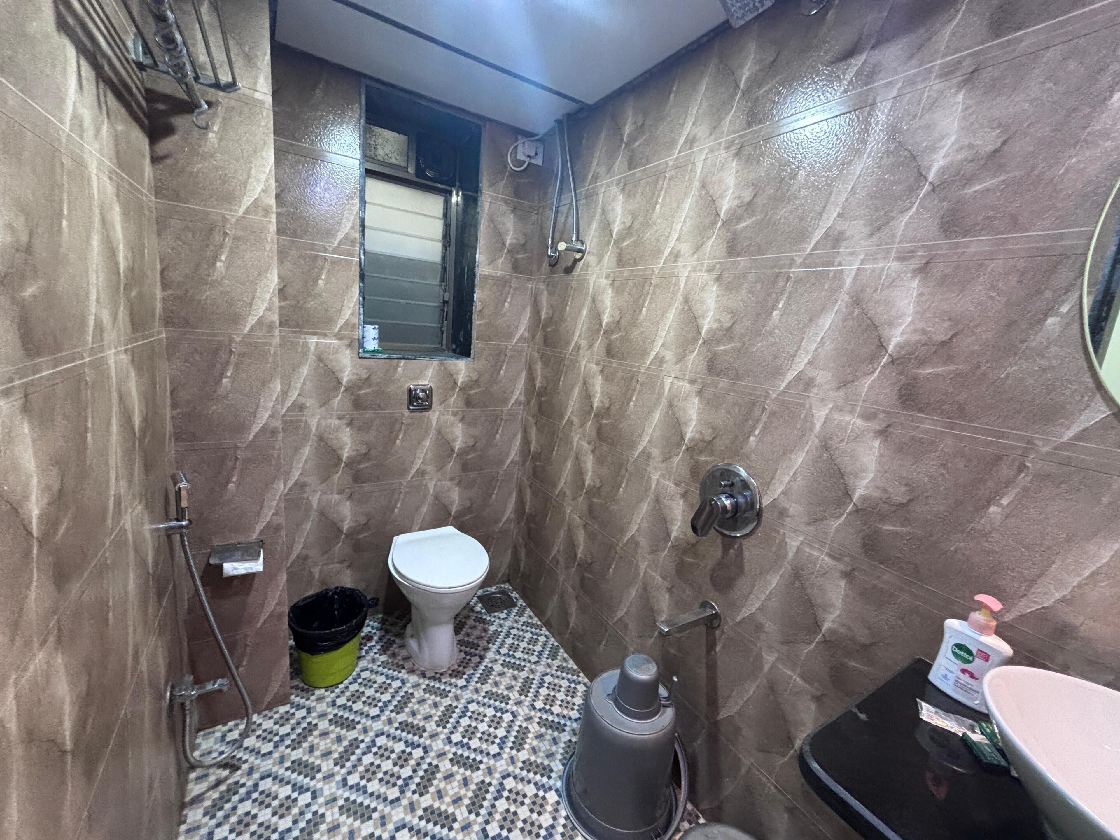 Un baño con inodoro, bidé, ducha, suelo de baldosas y un ventanal pequeño.