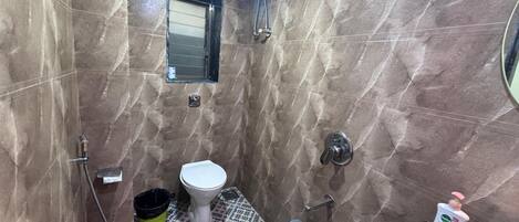 Un baño con inodoro, bidé, ducha, suelo de baldosas y un ventanal pequeño.
