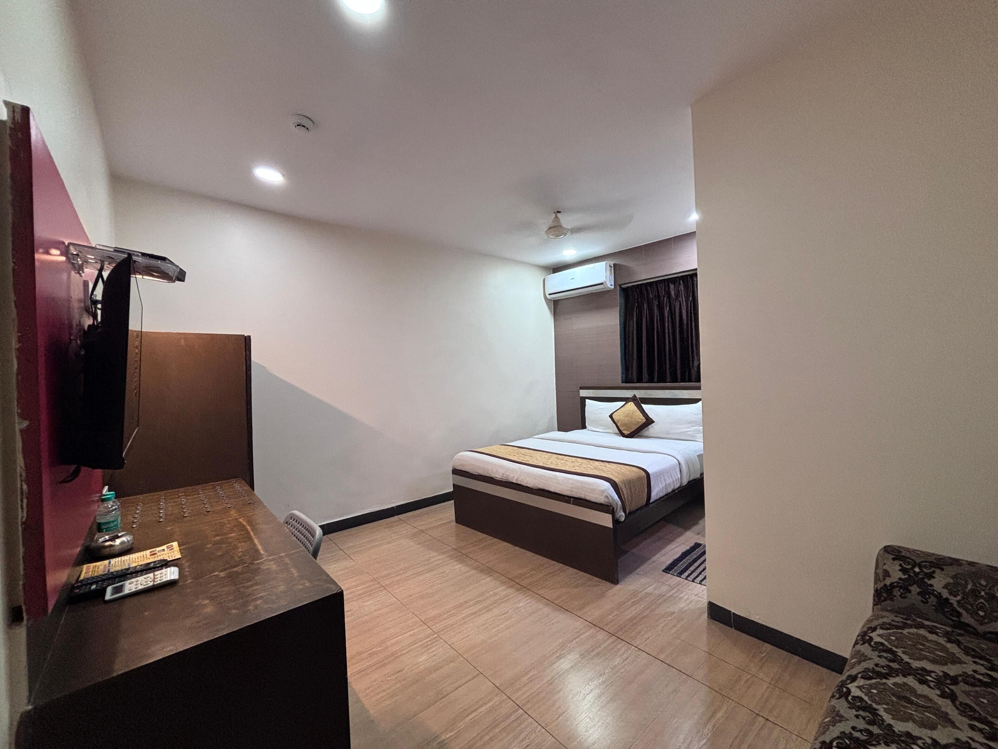 A hotel room with a bed, a desk with a television, a ceiling fan, and an air conditioning unit.