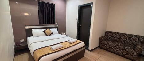 A hotel room with a bed, a sofa, an air conditioning unit, and a door.