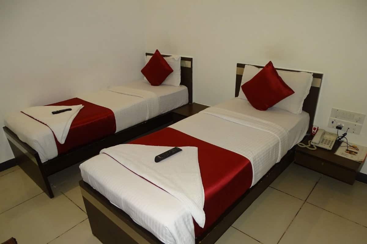 A hotel room with two single beds, each with a red pillow and a remote control on the bed.
