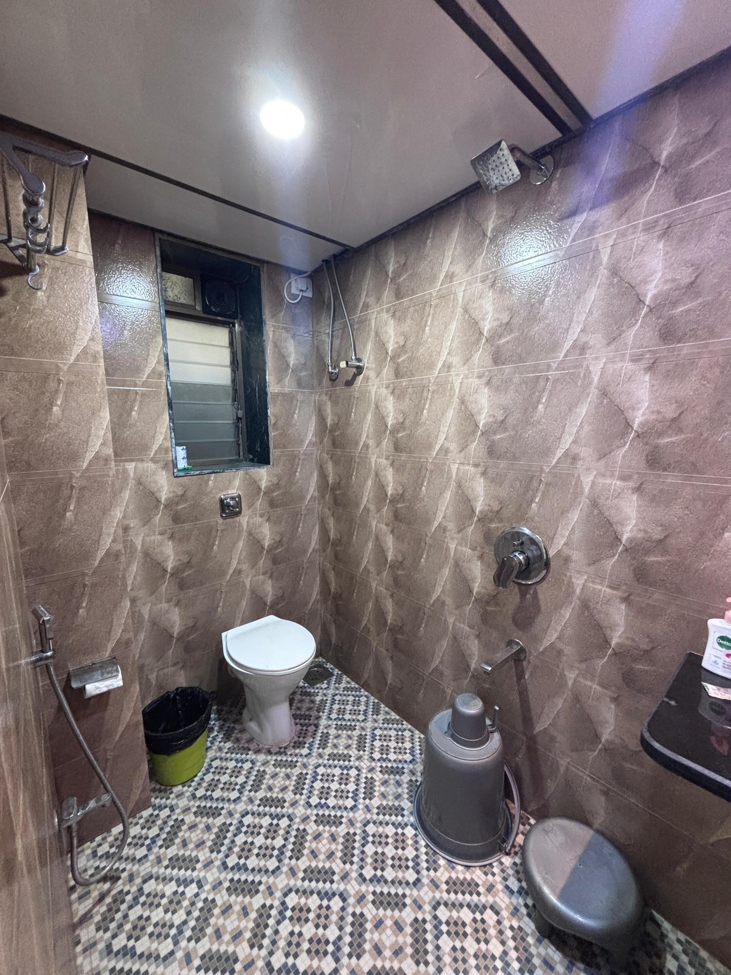 A bathroom with a toilet, bidet, shower, and a small window.
