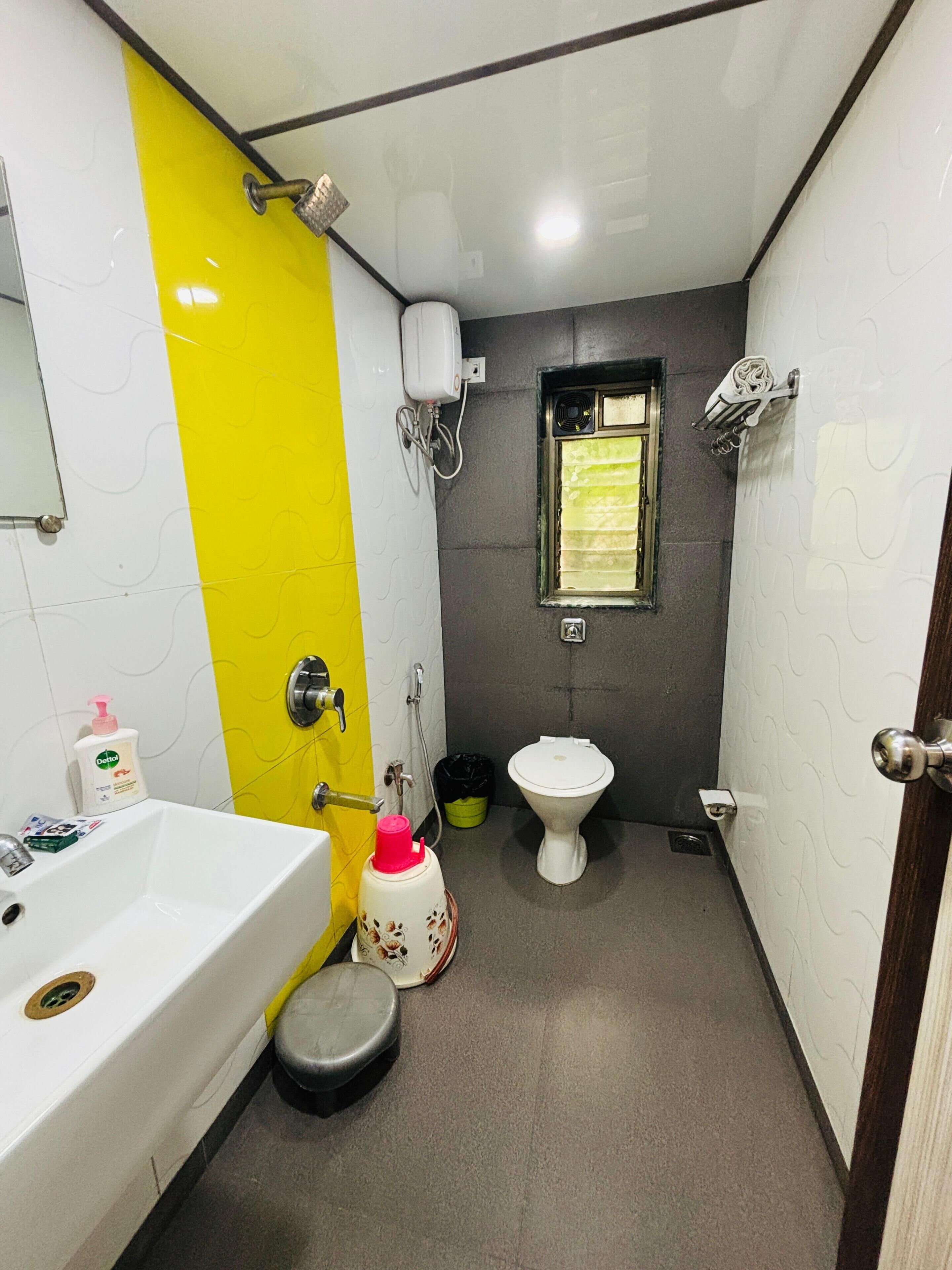 A bathroom with a white sink, yellow accent wall, a toilet, and a shower area.