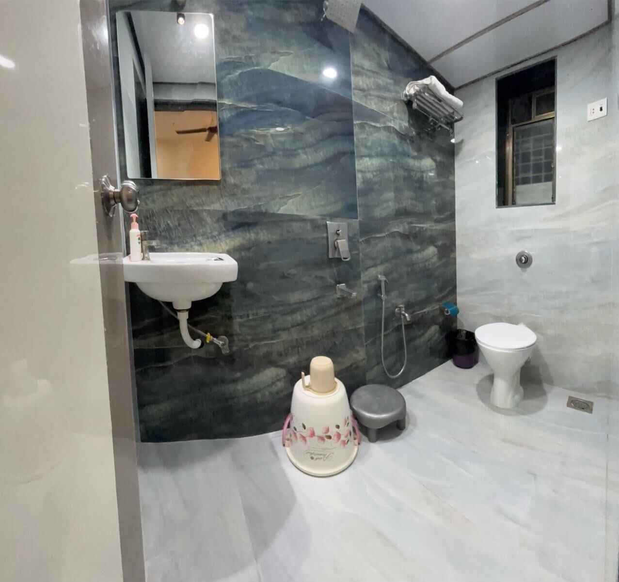 A modern bathroom with a marble wall, a sink, a toilet, and a shower.