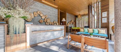 Una zona de recepción con un mostrador de madera, un banco y una pared decorada con discos de madera y una planta colgante.