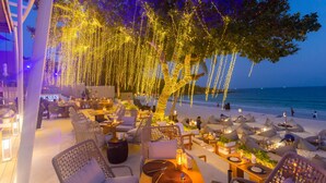 An outdoor dining area with tables and chairs, string lights, and a view of the beach.