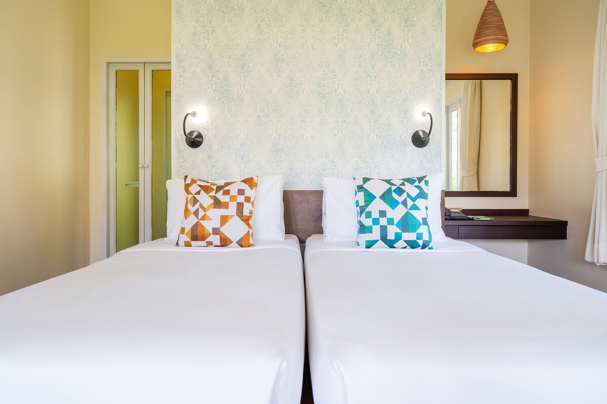 A double bed with patterned pillows, a bedside table, a mirror, and a hanging light fixture.