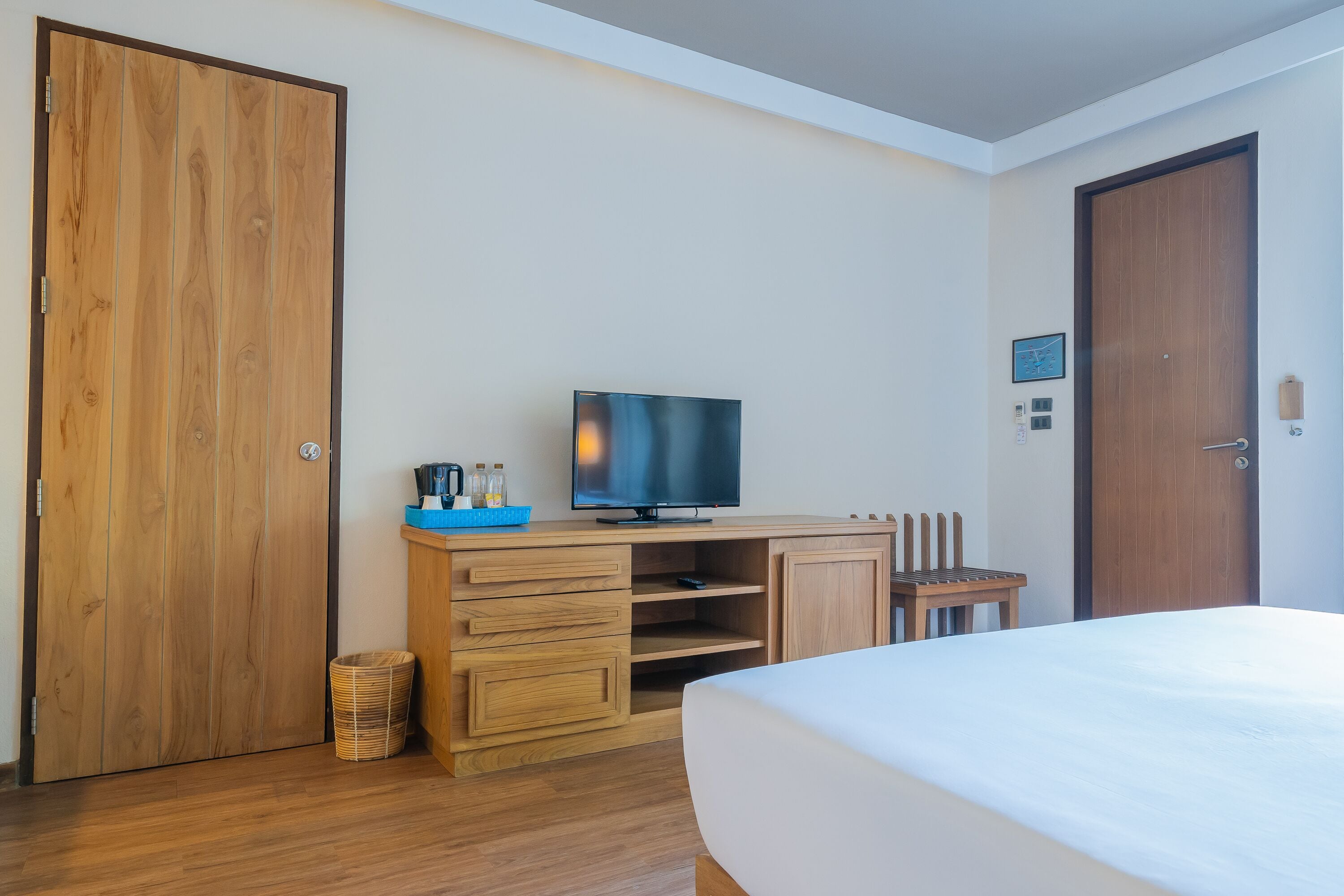 A hotel room with a wooden wardrobe, a television on a wooden stand, a bed, and a small wooden chair.