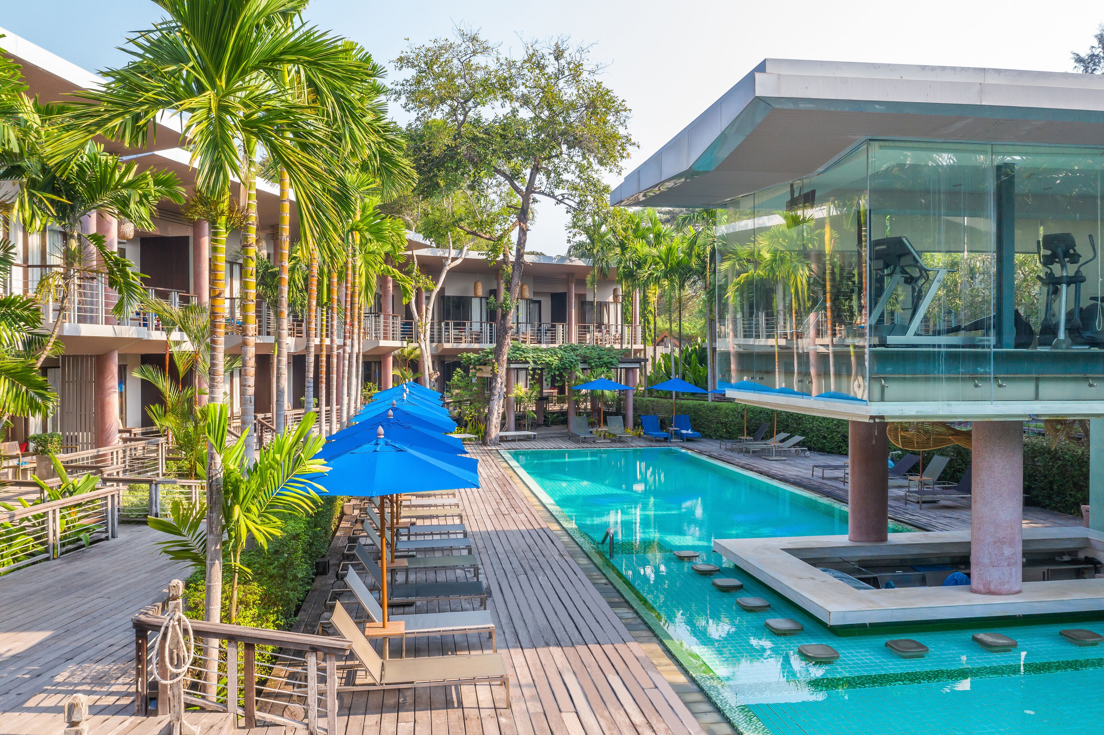 A hotel with a swimming pool, palm trees, and a glass-enclosed area with exercise equipment.