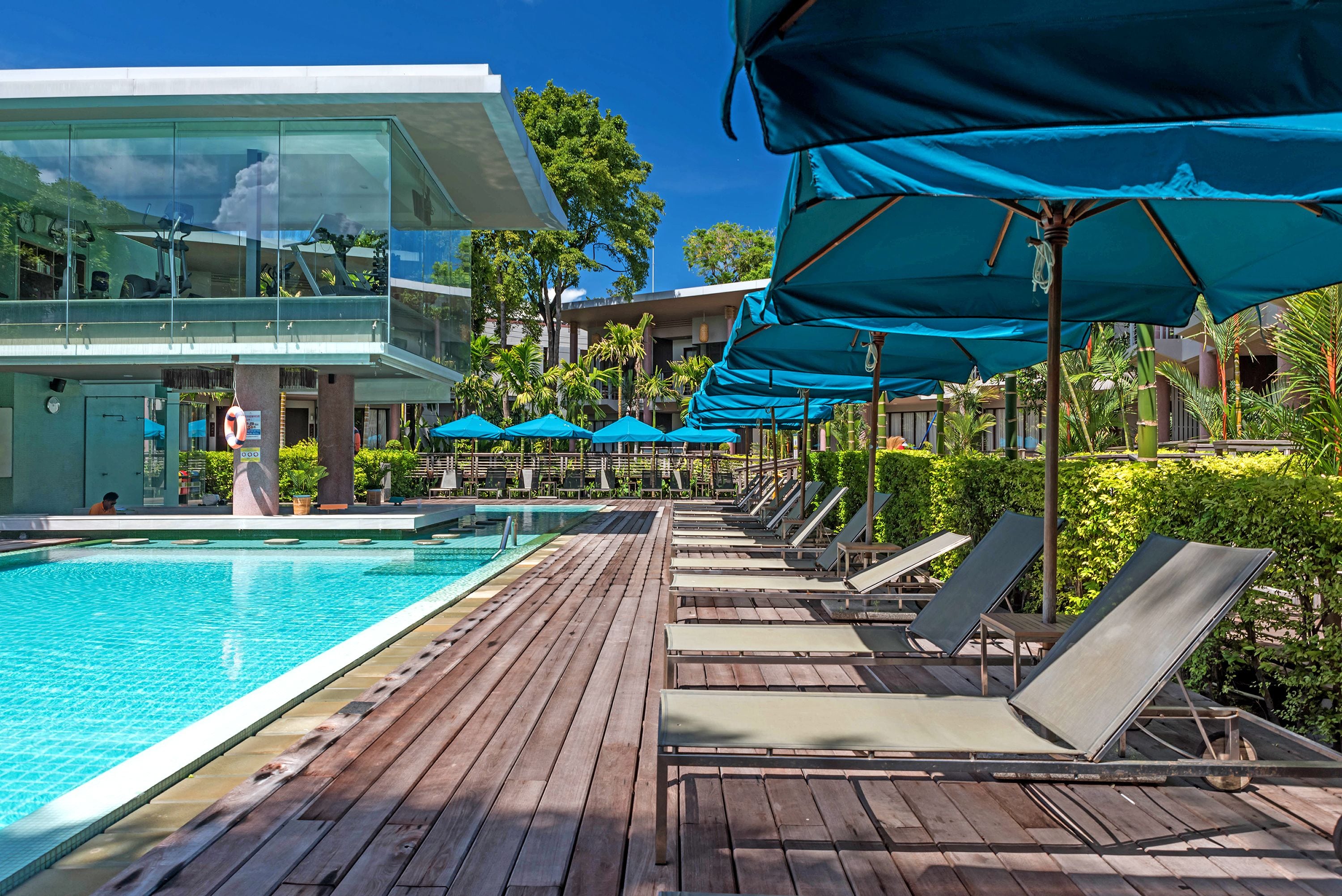 A poolside area with lounge chairs and umbrellas, a clear blue sky, and a modern building with glass windows.