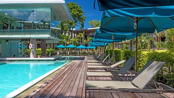 A poolside area with lounge chairs and umbrellas, a clear blue sky, and a modern building with glass windows.