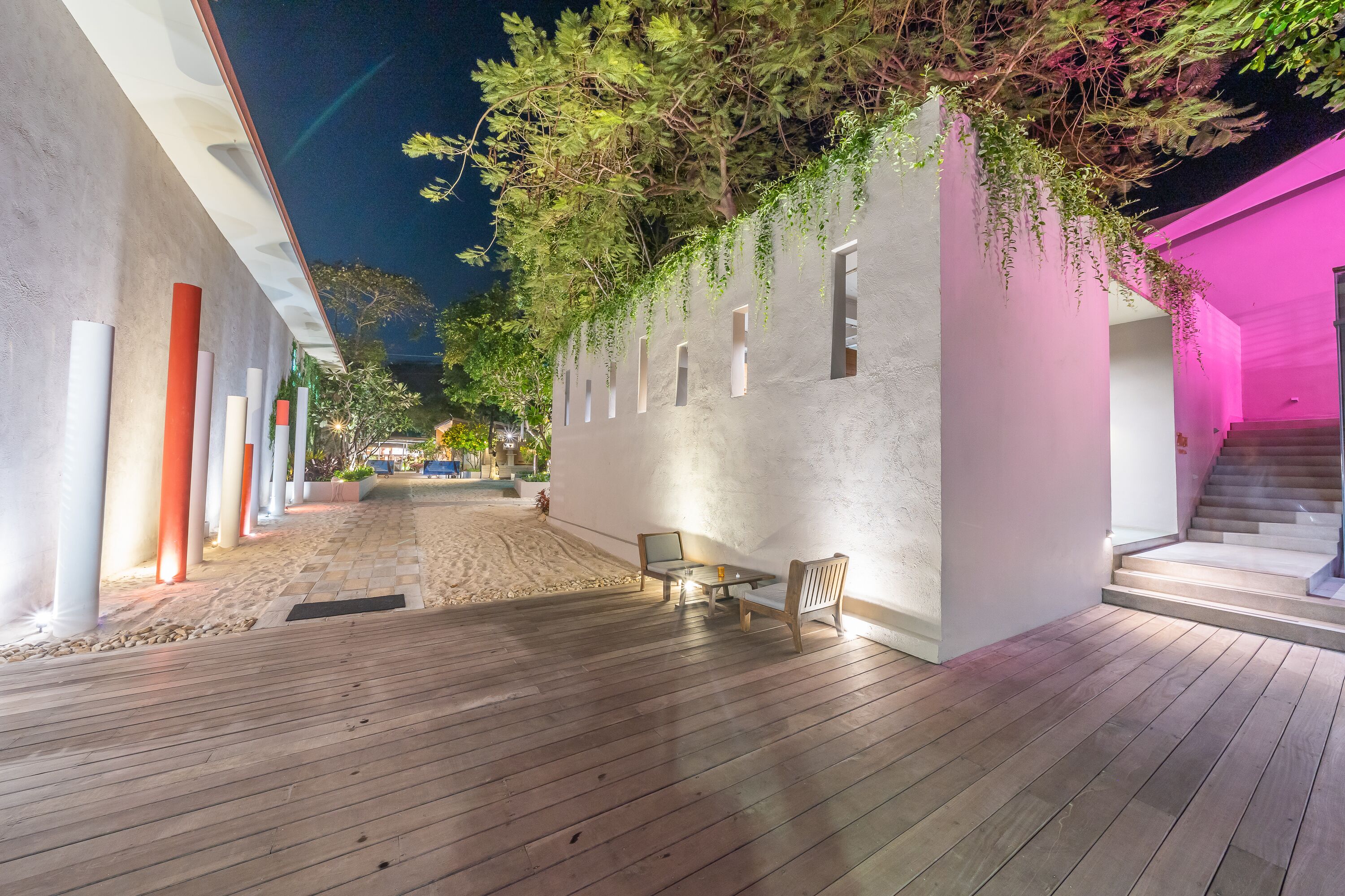 A covered outdoor area with a wooden deck, a seating area with two chairs, and a wall with hanging plants.