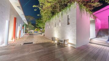 A covered outdoor area with a wooden deck, a seating area with two chairs, and a wall with hanging plants.