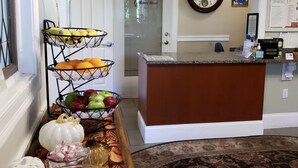 Un hall d’hôtel avec un comptoir d’accueil, un panier de fruits, une horloge et un panneau d’affichage.