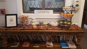 Un comptoir d’accueil avec une pancarte de bienvenue, un panier de fruits, un certificat TripAdvisor et un présentoir à livres.