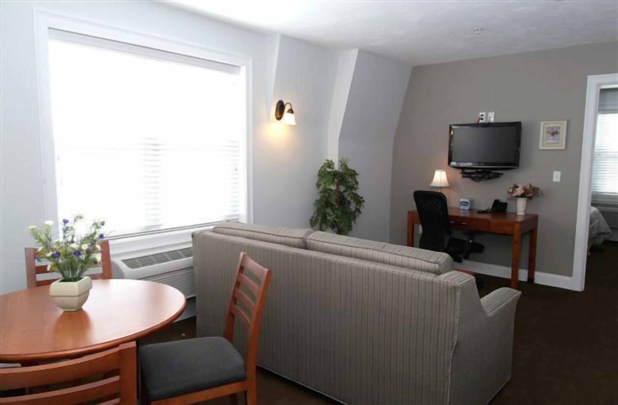 Uma sala de estar com sofá, uma mesa de jantar com cadeiras, televisão e uma planta.