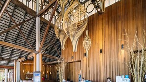 Un vestíbulo amplio con techo alto, paneles de madera y lámparas de mimbre modernas. Hay una recepción y un área de estar con un sofá de textura única.