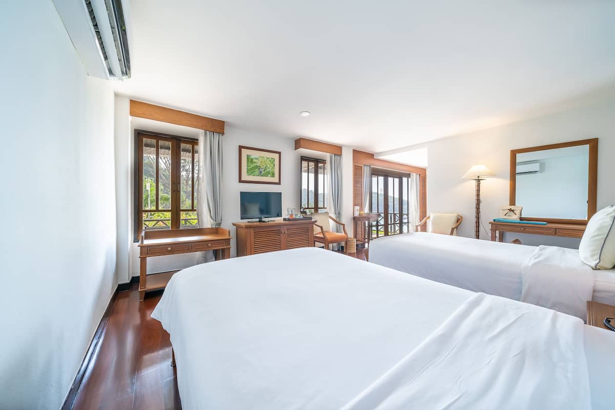 A hotel room with two beds, a desk, a television, and a large window.