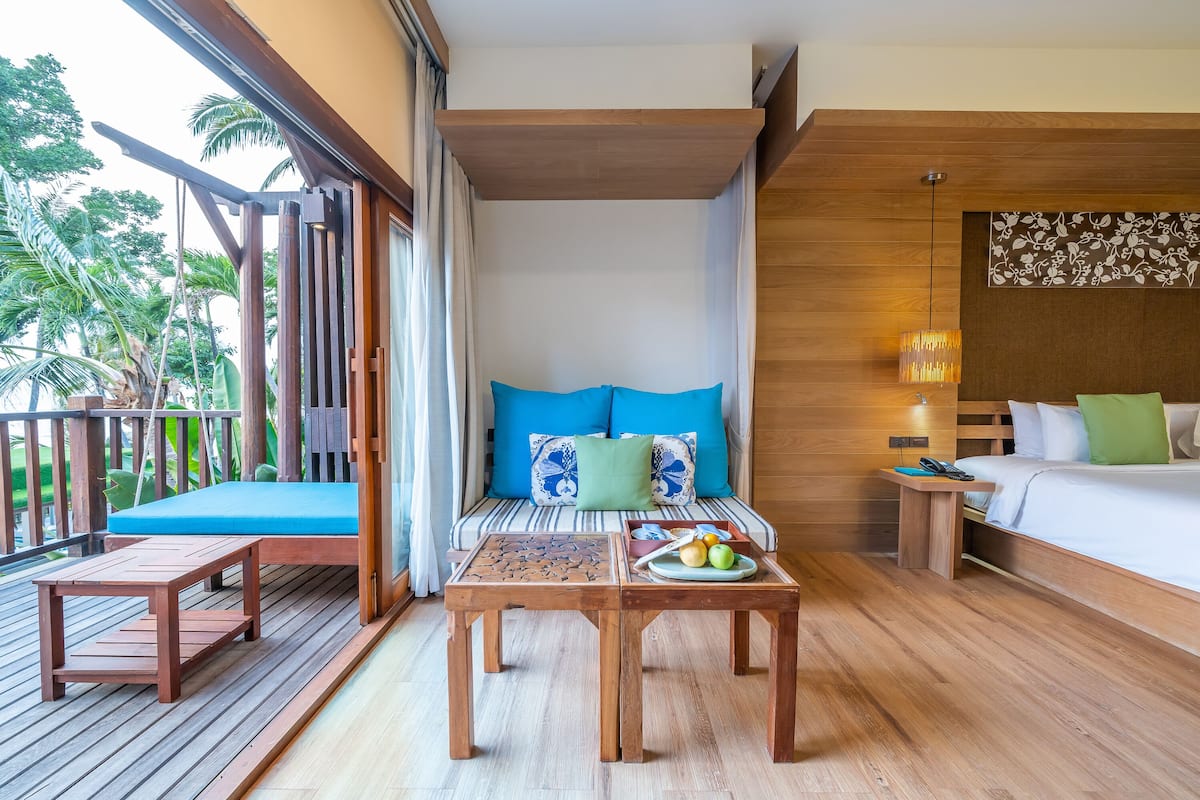 A wooden deck with a sofa and a table, a bed with pillows, and a wall with a floral design.