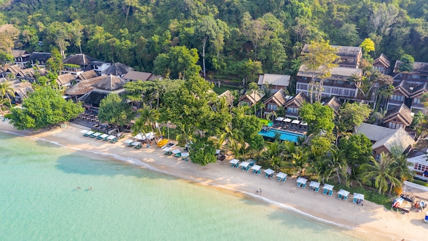 Vista aérea de un complejo turístico costero con villas frente a la playa, una playa arenosa y exuberante vegetación.