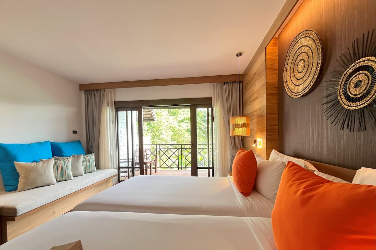 A hotel room with two beds, a sofa, a balcony, and a wooden wall with decorative items.