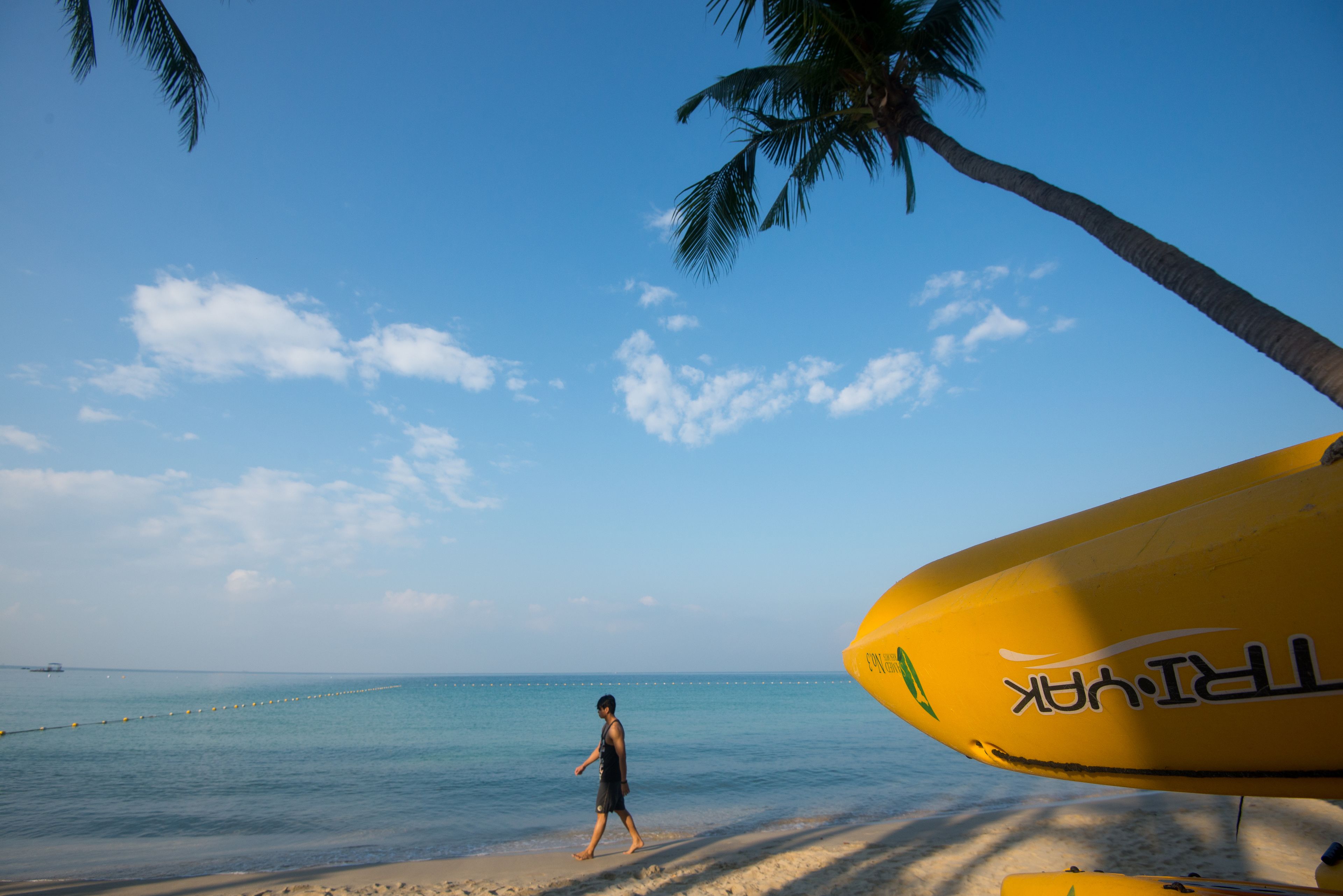 A beach scene with a clear sky, a person walking, and a yellow surfboard.