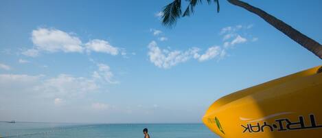 A beach scene with a clear sky, a person walking, and a yellow surfboard.