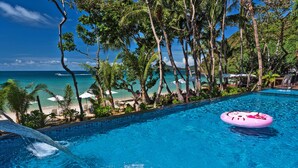 Una piscina con un flotador rosa, rodeada de palmeras y vistas a la playa.