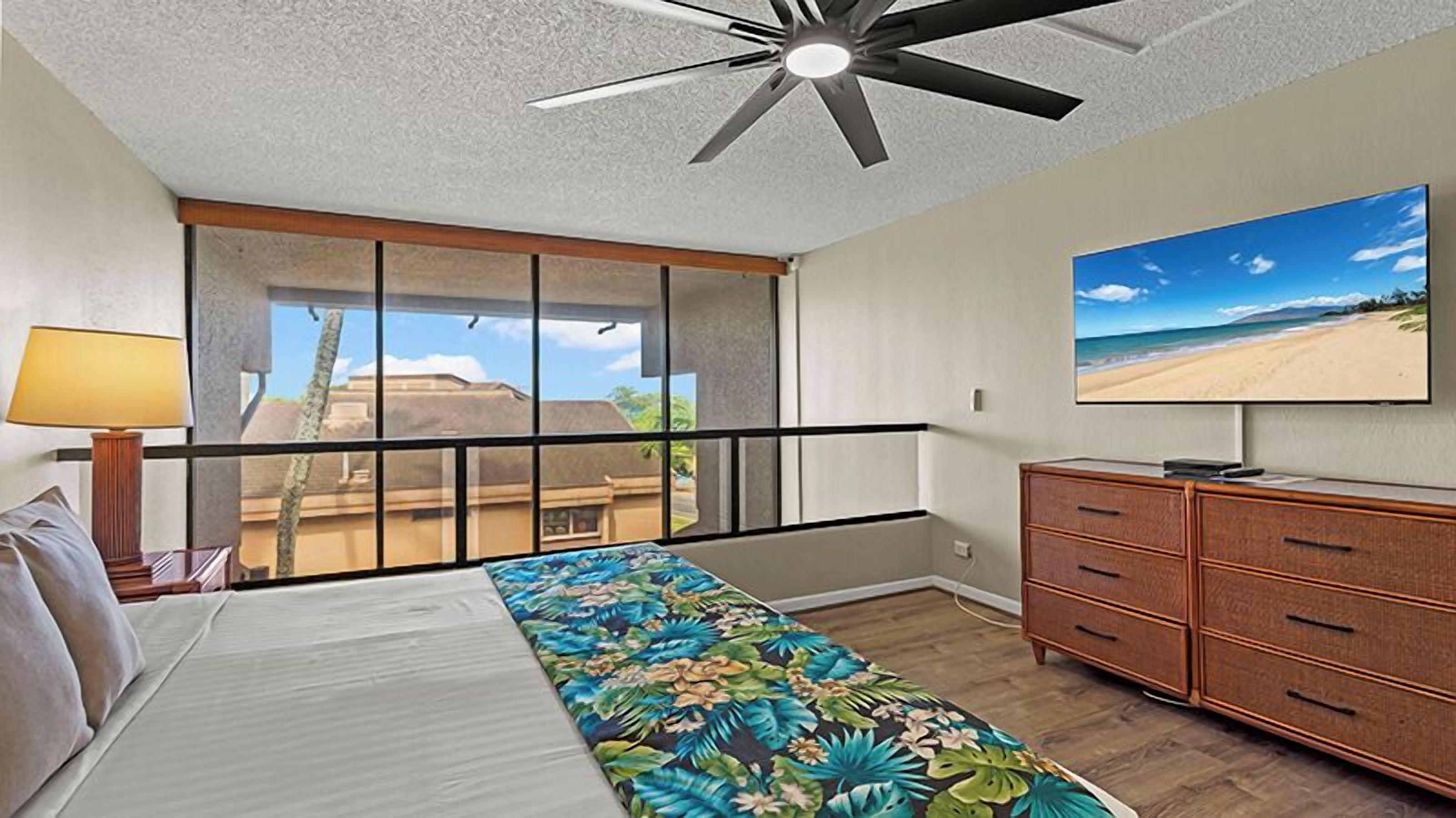 A hotel room with a bed, a dresser, a television, and a window with a view of a beach.