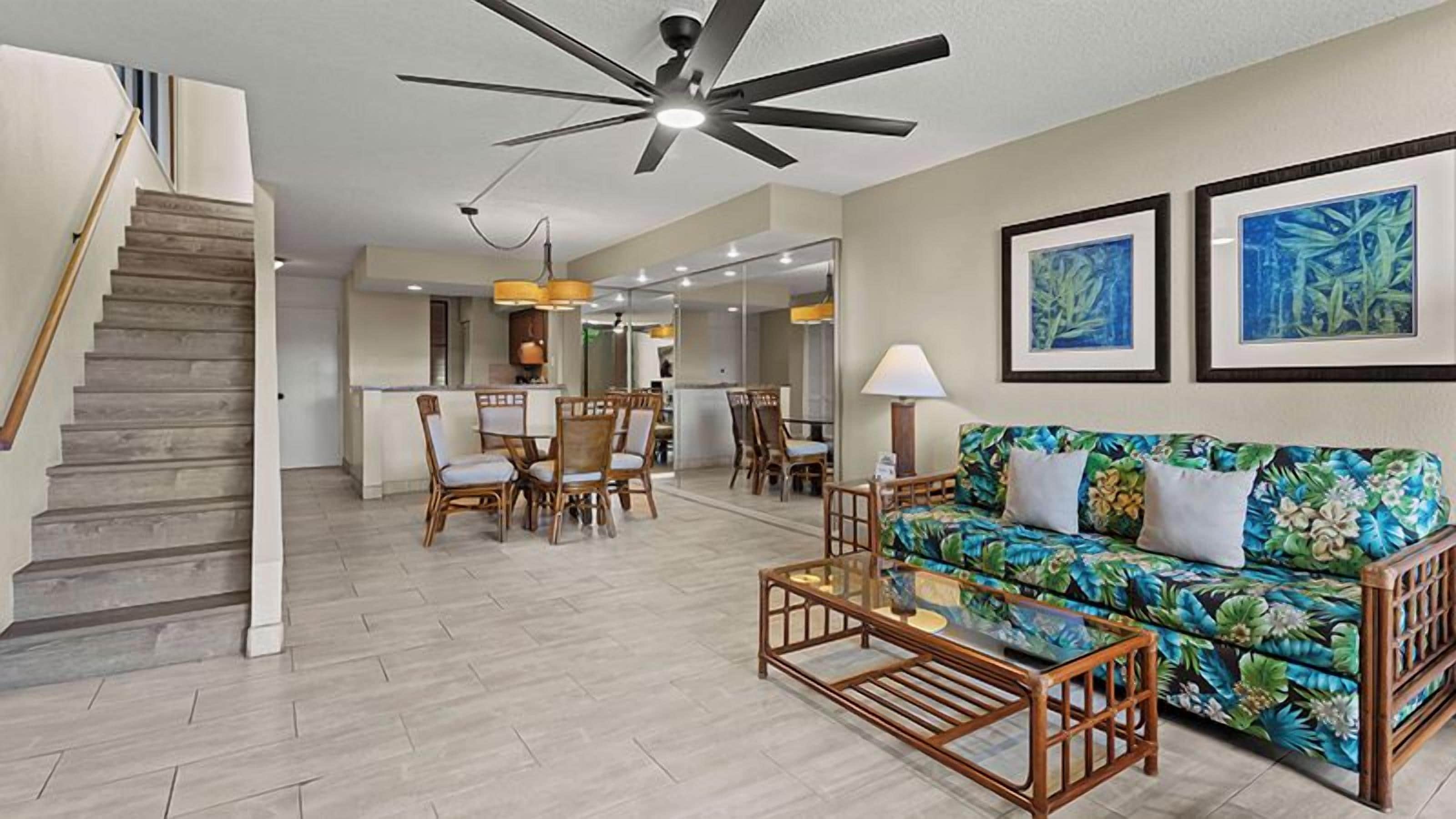 A spacious living area with a staircase, a dining table with chairs, a sofa, and a ceiling fan.