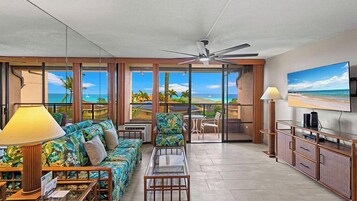 Habitación de hotel con balcón, un conjunto de sofás, televisor y comedor.