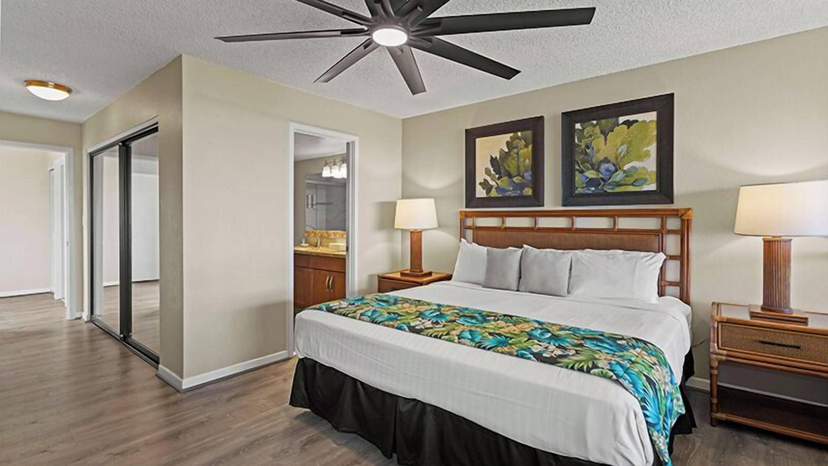 Une chambre d’hôtel avec un lit, des tables de chevet, un ventilateur de plafond et des œuvres d’art accrochées au mur.