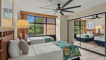 Habitación de hotel con dos camas, ventilador de techo, ventana grande y vista a la vegetación.