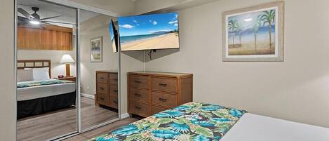 A bedroom with a bed, a TV, a dresser, a mirror, and a beach-themed painting.